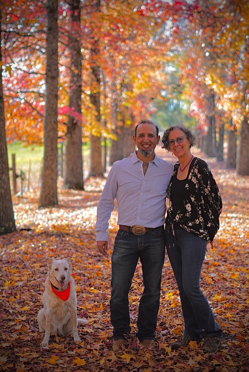 Vincent and Christine Hernandez with their dog Hazel, standing among autumn trees